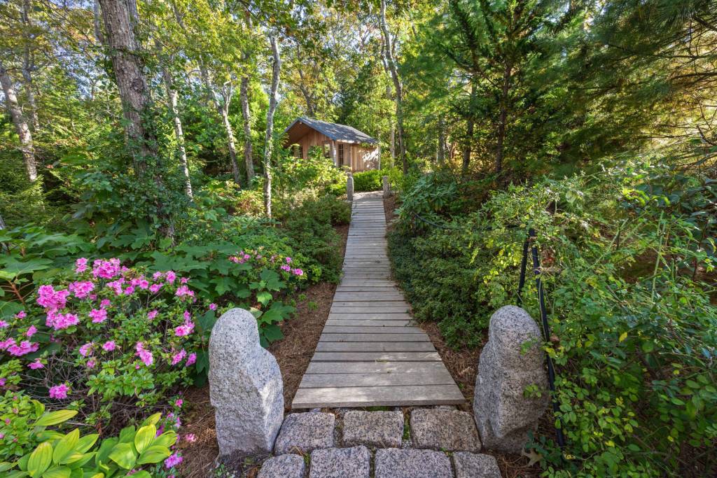 wood plank path surrounded by greenery leading to an outdoor sauna building
