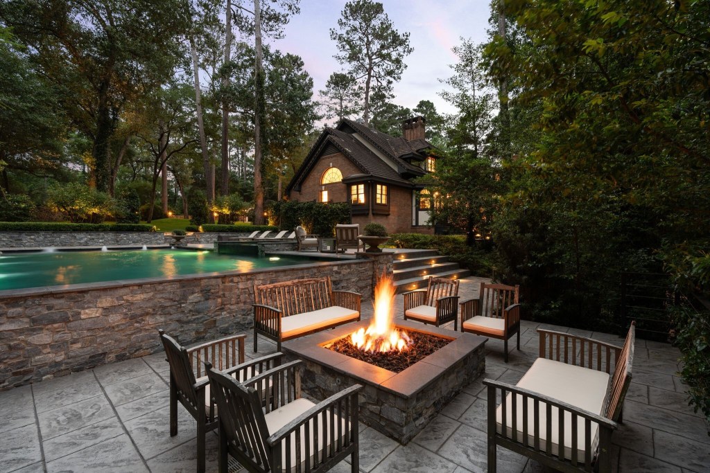 fire pit with outdoor seating, multi-level patios with pool and Tudor-style home in background