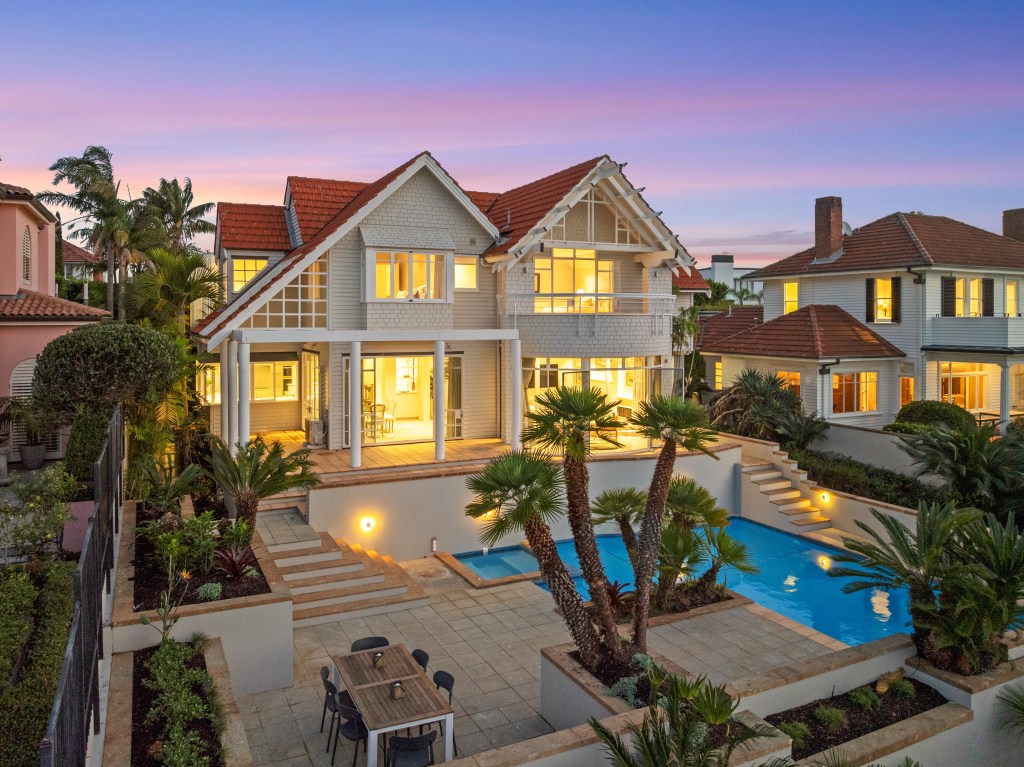 Back facade and pool of a shingle-style home in Aukland, New Zealand, at susnset.