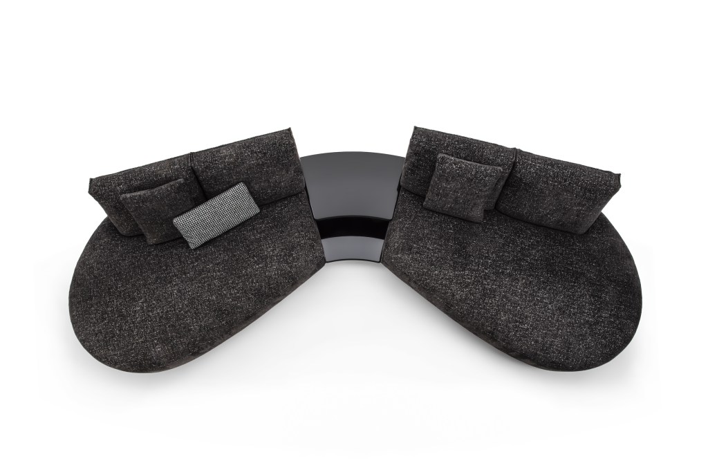 Overhead view of a dark charcoal curved modular sofa with accent cushions, arranged in two sections around a matching curved table on a light background.