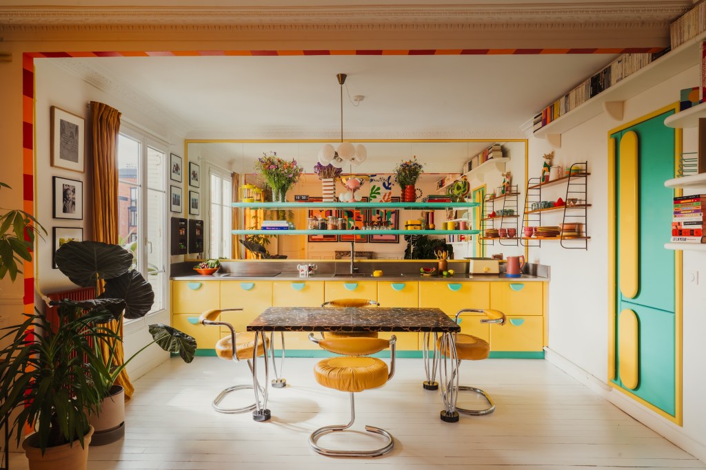 Bright contemporary kitchen with yellow and turquoise cabinetry, open shelving, a black dining table with upholstered stools, and colorful decorative accents throughout the space.
