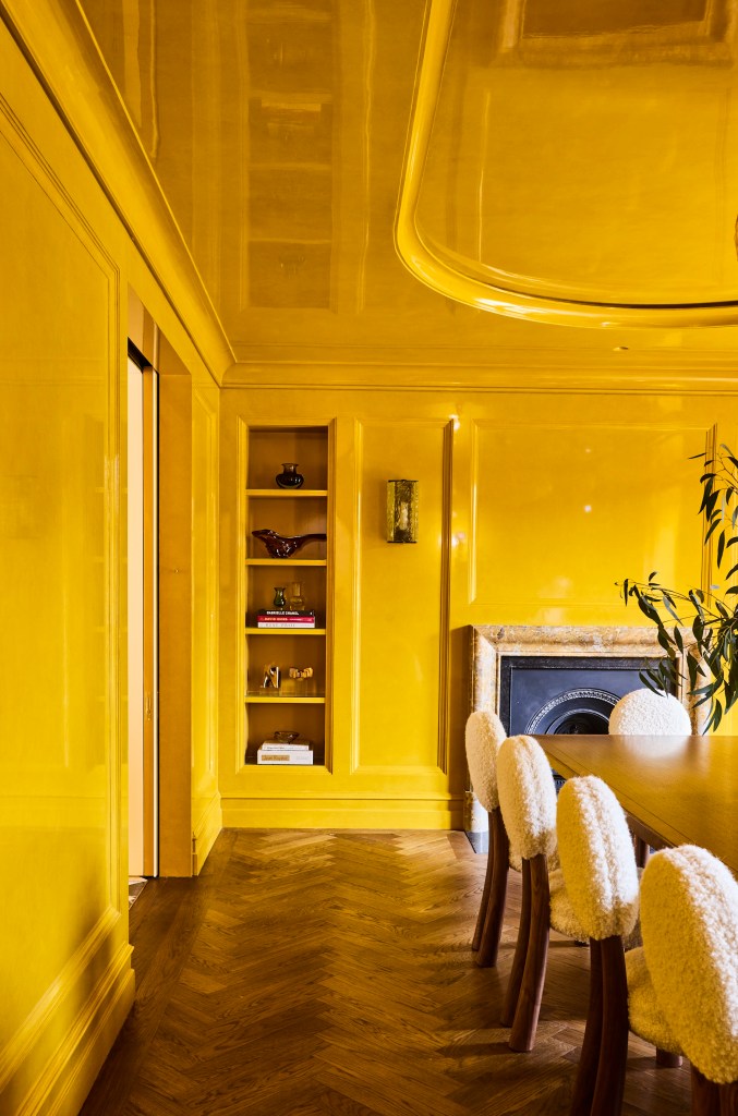 Dining room with glossy yellow walls and ceiling, herringbone wood flooring, a wooden dining table, upholstered chairs, built-in shelving, and a fireplace.
