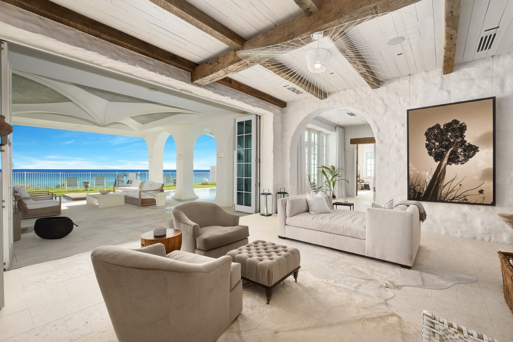 Elegant oceanfront living space featuring vaulted wood-beam ceilings, indoor-outdoor design, and direct views of the terrace and coastline.