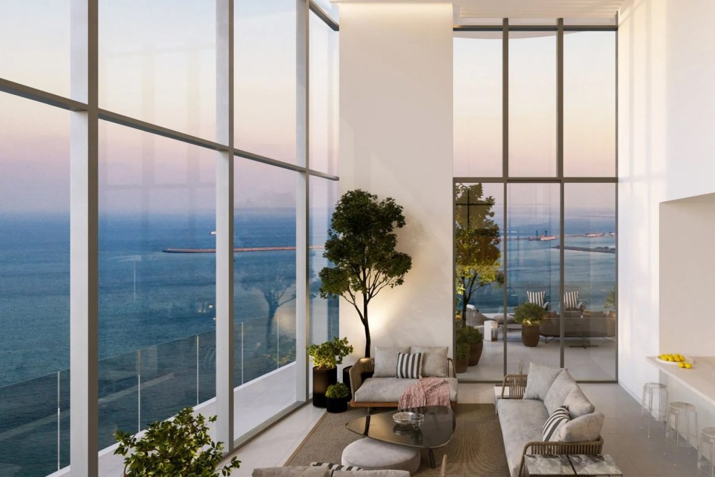 Elegant double-height living room with floor-to-ceiling windows showcasing panoramic sea views, modern furnishings, and a bright open design. Limassol, Cyprus.