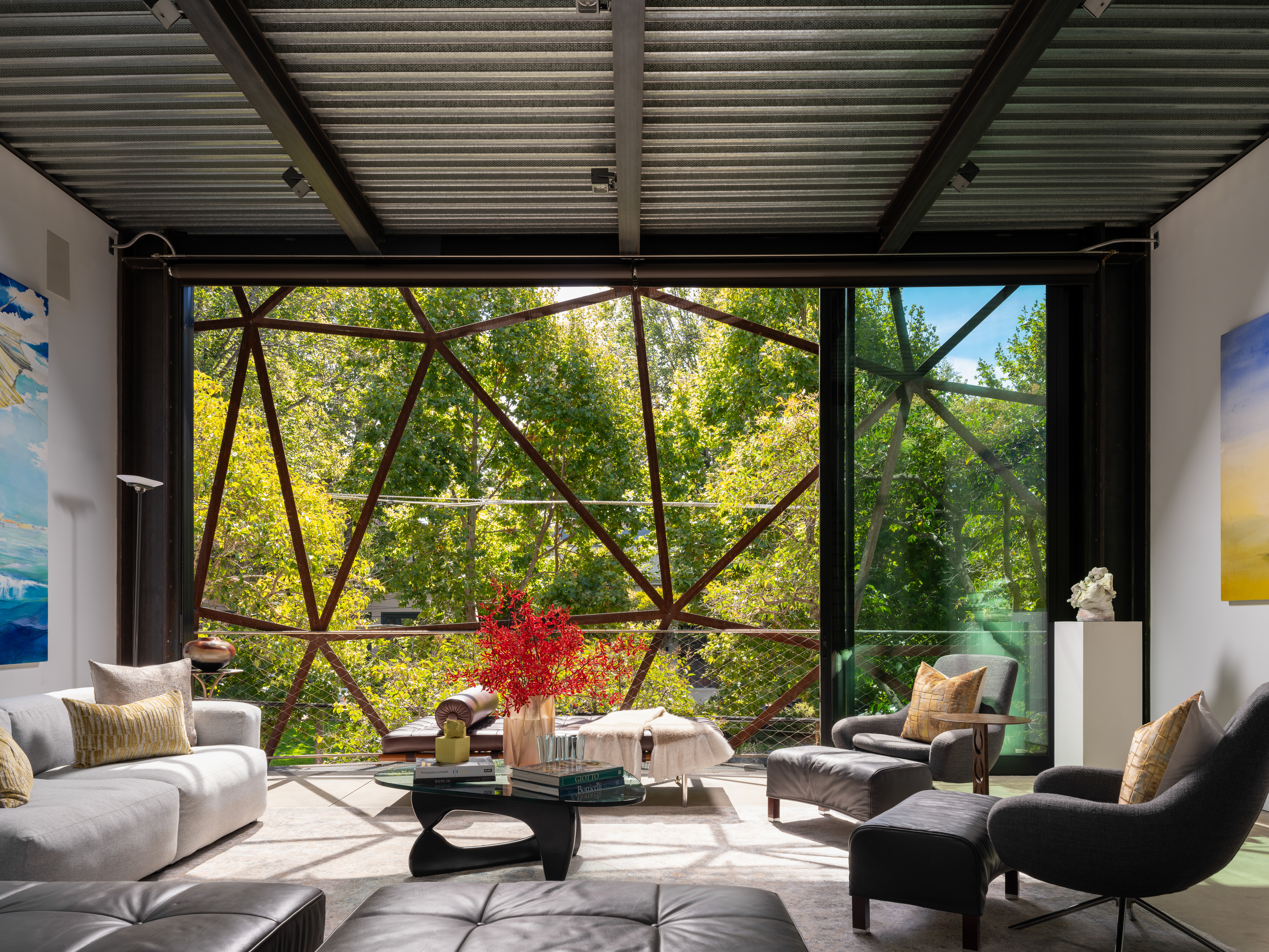 interior of Gallery House in San Francisco sitting room, with sofa, chairs, coffee table, and walls lined with art. Facing a sliding window with artistic metal webbing overlooking trees
