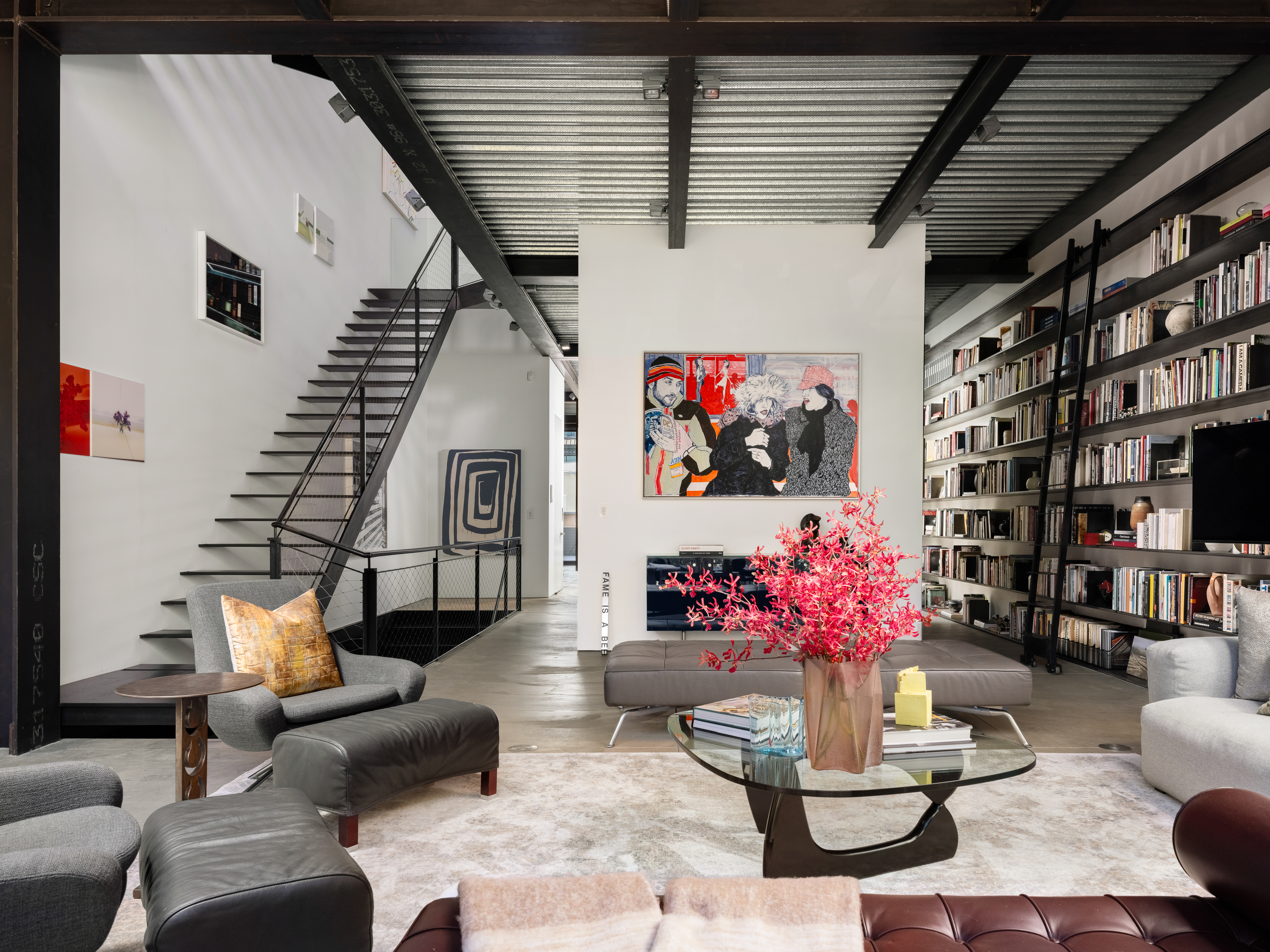 Interior of San Francisco's Gallery House sitting area, with large metal staircase, expansive bookcases, and freestanding wall with large art piece in the background