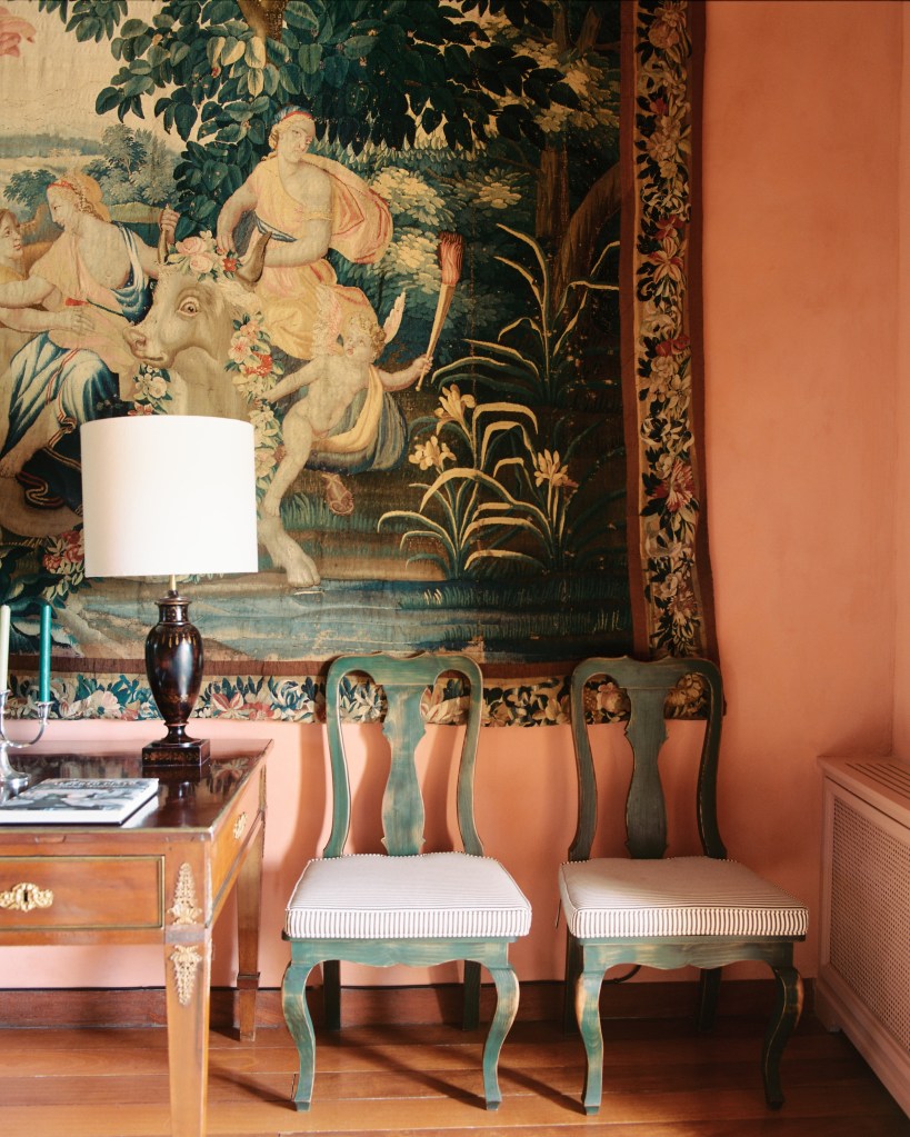 Antique tapestry depicting a cherub and the Queen of Sheba in an outdoor setting against a terracotta wall in a Spanish home