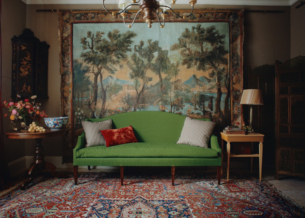 seating area with green sofa and two side tables, with large antique tapestry in the background depicting an outdoor scene
