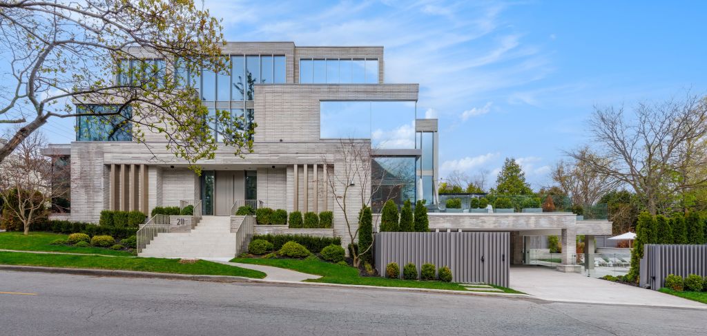 Contemporary three-story residence with a light stone exterior, expansive floor-to-ceiling windows, landscaped grounds, and a covered driveway viewed from the street.
