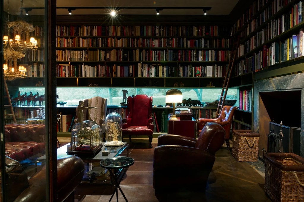 moody salon in New South Wales home, with raised library bookshelves, marble fireplace, traditional leather seating, and curios adorning the coffee table