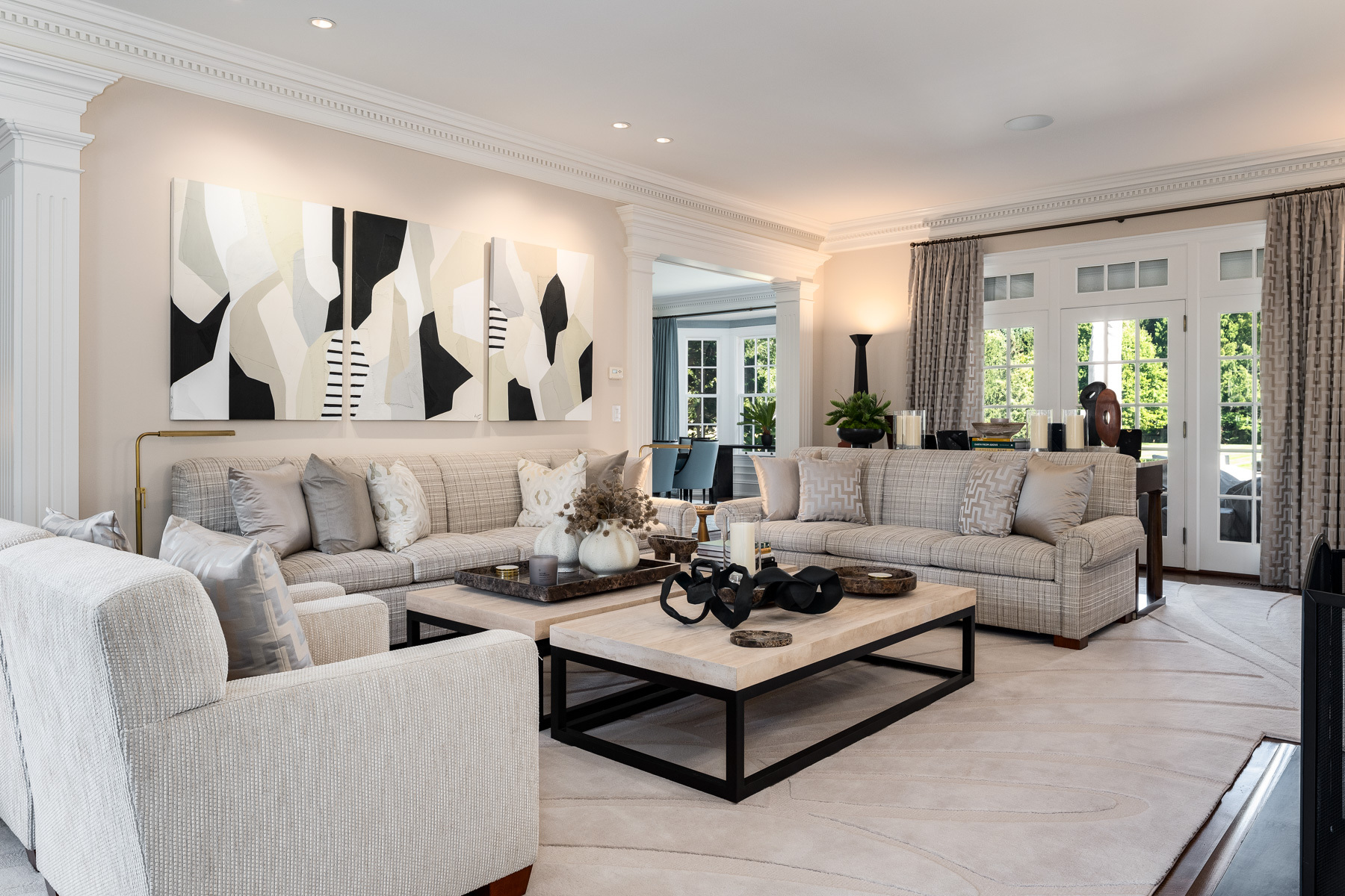 grey and white living room with three sofas, two black and white coffee tables, various art and sculptural works set on the tables, and three cohesive black, white, and grey paintings on the wall behind