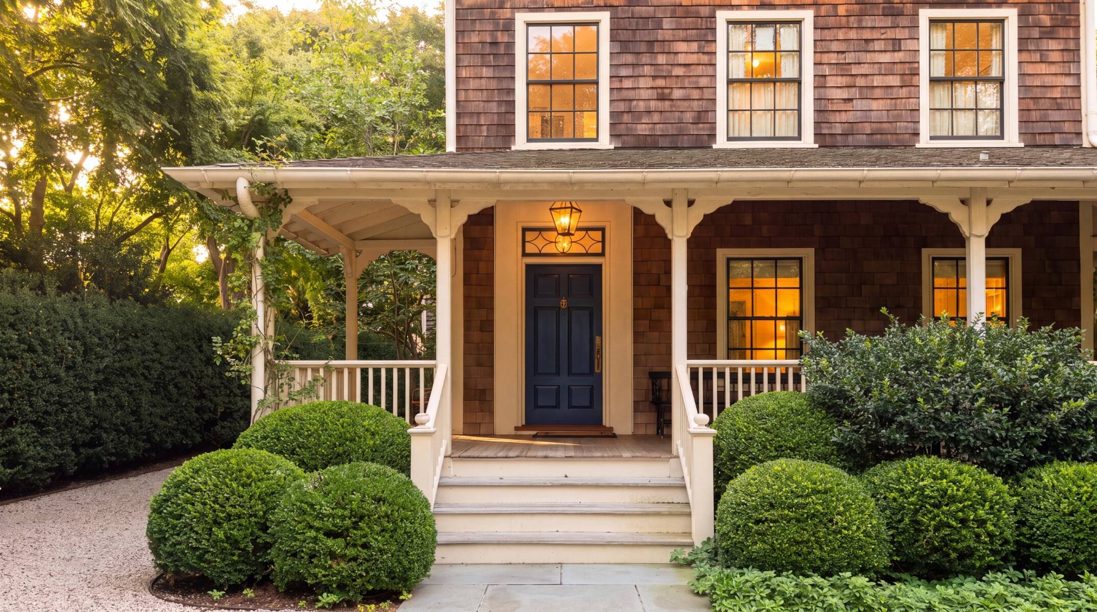 exterior photo of Sag Harbor, NY historic home with wraparound porch, manicured landscaping, and a close up of a blue front door