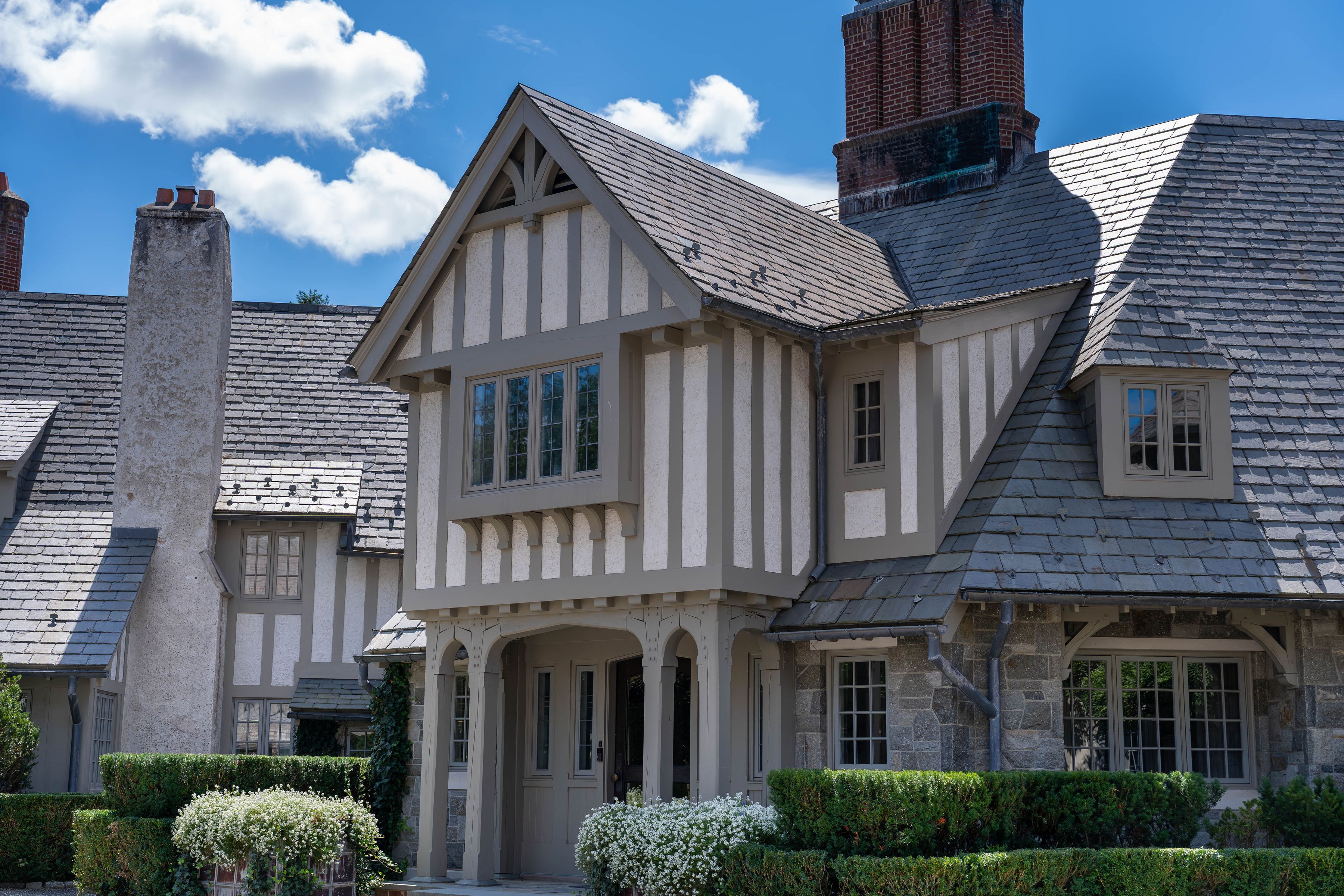 exterior of grey and white Tudor-style home in Greenwich, CT showcasing the front door, pitched rooflines, and windows