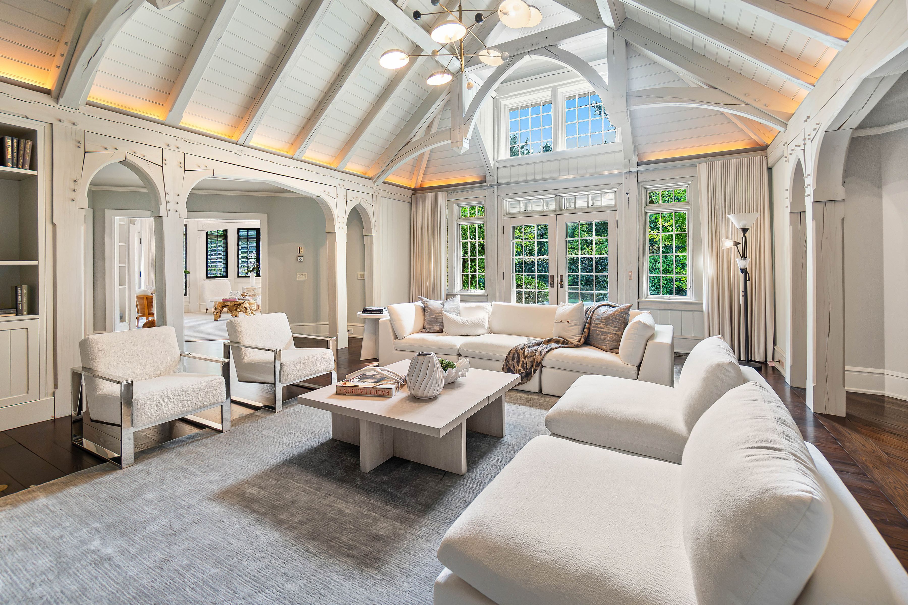 all white sitting room with vaulted ceilings, large french doors, two plush sofas and two chairs, and a solid wood coffee table