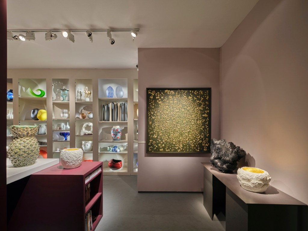 various collectibles on display at Adrian Sassoon's stand at PAD in London 2025, featuring a large, gallery-lit painting, several sculptures and ceramics, and a wall of other displayed art pieces