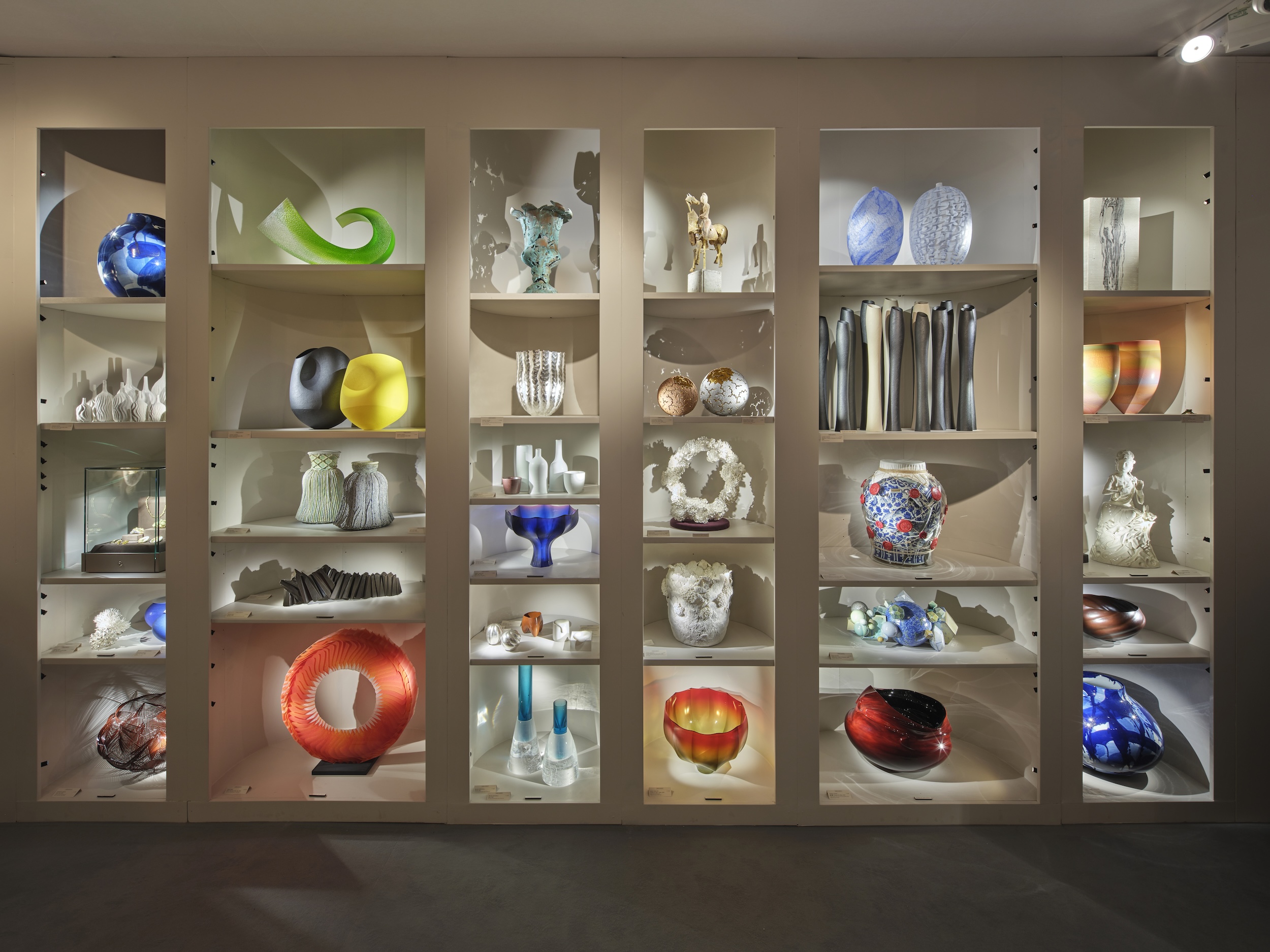 photograph of an Adrian Sassoon display of 31 curated art pieces in backlit custom shelving, displayed in London's PAD