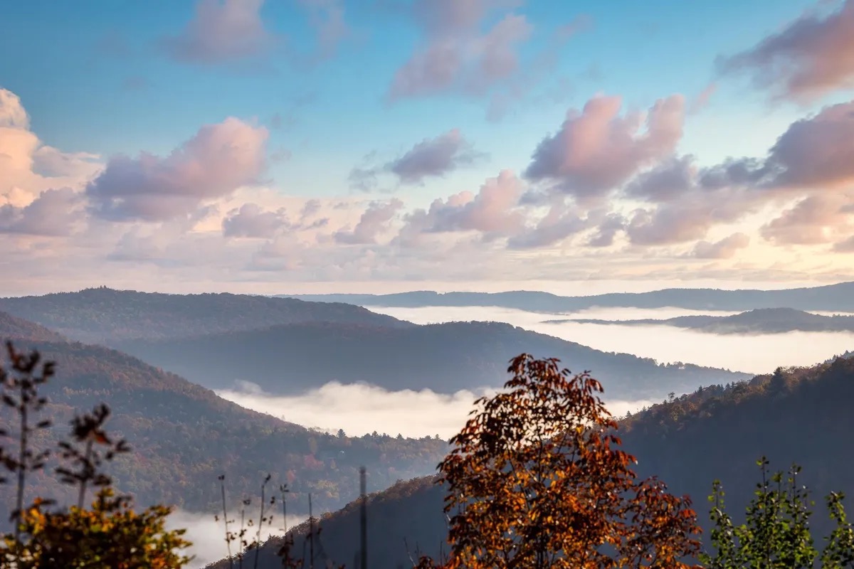 panoramic photo across mountains in Killington, Vermont, with rolling fog and trees with changing leaves for autumn, set against a cloudy sky backdrop