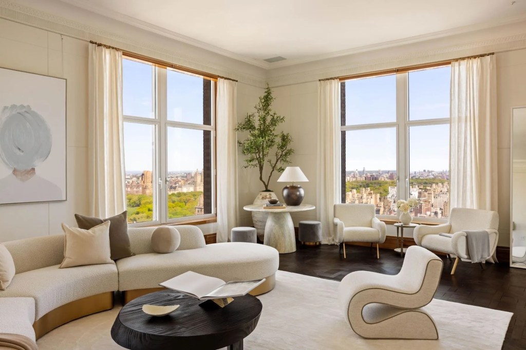 monochromatic sitting room, with sculptural, plush seating, wood coffee table, marble side table, and large windows looking out across New York City