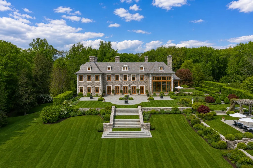Front elevation of a two-story stone Georgian-style estate with symmetrical architecture, landscaped grounds, and a circular gravel motor court.